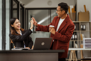 Middle-aged businessman and young Asian businesswoman diligently working at desks, managing tasks as recruitment, training, performance management, inclusive organizational culture.
