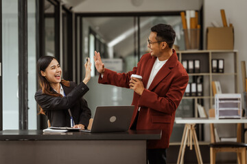 Middle-aged businessman and young Asian businesswoman diligently working at desks, managing tasks...