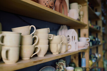 No people shot of handmade cups and earthenware on shelves in pottery workshop, copy space
