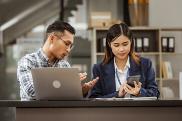 Fototapeta premium A middle-aged businessman, a young businesswoman, and Asian individuals are collaborating at desks. They engage in teamwork while managing commodities, trade, finance, and talent acquisition.