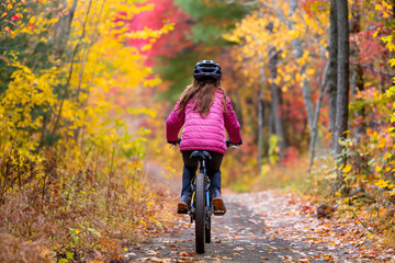 Fototapeta premium Young girl enjoying a peaceful autumn cycling adventure through the vibrant and colorful forest trail. Surrounded by the stunning fall foliage and scenic nature
