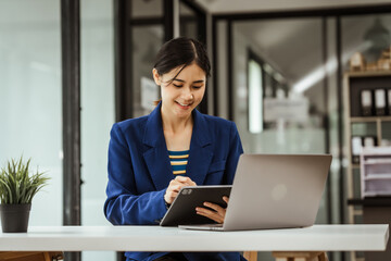 Young woman and other Asian individuals in formal suits working at desks with laptops. They engage...