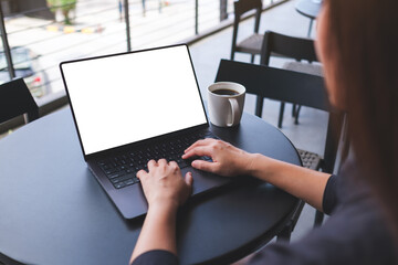 Mockup image of a woman working and typing on laptop computer with blank white desktop screen in...