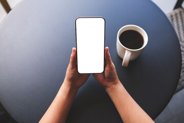 Top view mockup image of a woman holding mobile phone with blank screen with coffee cup on table