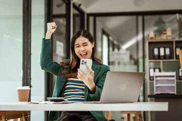Young woman and other Asian individuals in formal suits working at desks with laptops. They engage...