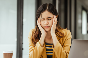 Fototapeta premium A young woman and other Asian individuals in formal suits are seen working at desks with laptops, facing challenges such as burnout, anxiety, pressure, fatigue, and job dissatisfaction.