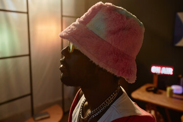 Side view close up of Black young man wearing fuzzy bucket hat in studio with dim lighting copy...
