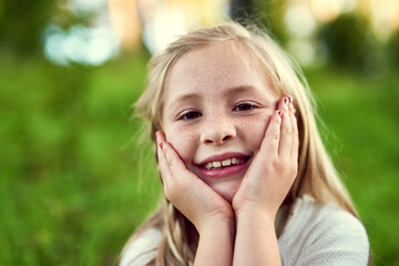 Fototapeta premium Girl, child and smile on grass with portrait outdoor for fun or playing, fresh air and enjoyment of youth or childhood in summer. Female kid, relax and nature in afternoon for carefree and adventure.