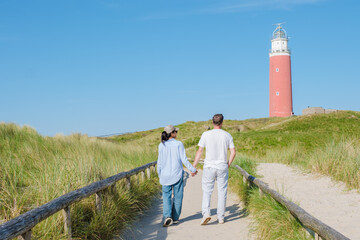 A couple leisurely walks along a path near a picturesque lighthouse on a bright sunny day in Texel,...