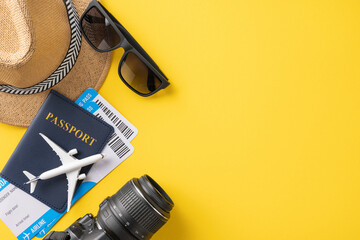 Flat lay shot of summer travel essentials including passport, airplane tickets, hat, sunglasses, and camera on vibrant yellow background