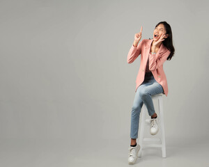 full lenght shoot of happy excited asian woman sitting on stool shouting with hand cupping gesture...