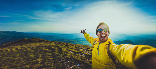 Young hiker man taking selfie portrait on the top of mountain - Happy guy smiling at camera - Tourism, sport life style and social media influencer concept