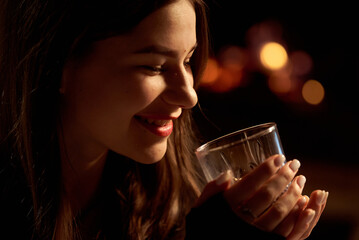 A beautiful young girl hugs a glass of alcohol in the evening in a restaurant.