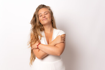 Young beautiful woman wearing casual dress over isolated white background hugging oneself happy and...