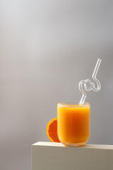 On a table, there is a glass of orange juice with a straw beside an orange slice