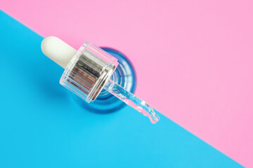 Bottle with serum and pipette on pink background close-up, top view.