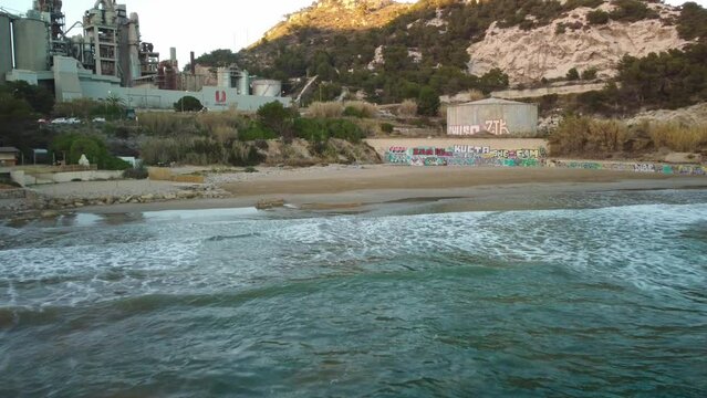 Costa garraf beach with waves, graffiti, and a factory in the background, aerial view