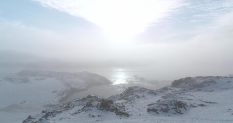Rise up shot over morning mist Antarctica coast. Majestic snow-capped mountain peaks above sunrise clouds. Fly over fog cloudscape. Ocean aerial view surface. Wild nature background. Drone flight