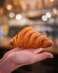 Obraz premium Hand Presenting a Perfectly Baked Croissant
