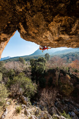 Girl climber on an overhanging rock. A sports woman climbs a rock against the backdrop of...