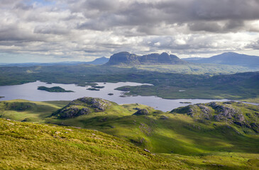 Views of the summits of Suilven, Caisteal Liath with Loch Sionasgaig below from the summit of Stac Pollaidh in the Scottish Highlands on a sunny summers day with dramatic clouds in the UK