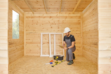 Construction man, builder man construct new wooden home, tiny house style. Spirit level, screw, tool bag and charged drill. Wood shelter style.