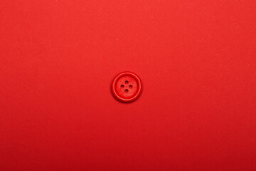 One alone red clothes button with four holes isolated on the bright solid fond plain red background