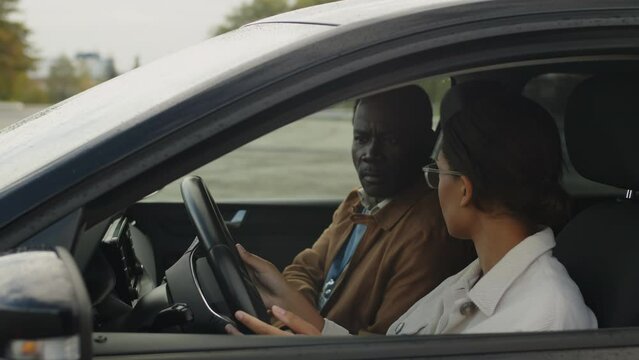 Medium shot of young African American female student holding steering wheel while sitting in car with mature Black male driving coach, reminding traffic rules before lesson