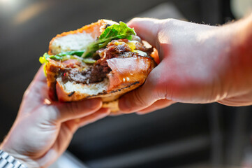 Close-up of a hand holding a half-eaten burger with visible layers of lettuce, cheese, and meat.