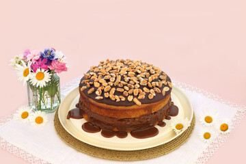 Peanut and caramel homemade cake decorated with peanuts and sauce on pink background with summer flowers. 