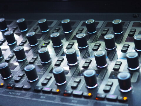 Close-up of illuminated black light mixer with rotary knobs and orange buttons at a festival.