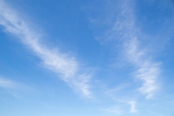 Diagonal lines of cloud surrounding a small moon against a blue sky