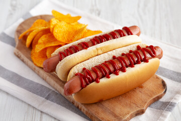 Homemade Hot Dog with Ketchup with Potato Chips on a Wooden Board, side view.