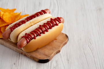 Homemade Hot Dog with Ketchup with Potato Chips on a Wooden Board, side view. Space for text.