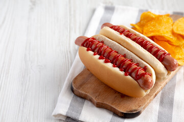 Homemade Hot Dog with Ketchup with Potato Chips on a Wooden Board, side view.