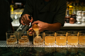 Barman pouring fresh juice into the glasses with whiskey and ice cubes for finishing cocktail on...