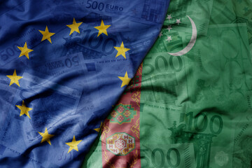 big waving realistic national colorful flag of european union and national flag of turkmenistan on a euro money banknotes background.