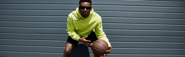 Handsome young African American man in green hoodie holding a basketball. © LIGHTFIELD STUDIOS