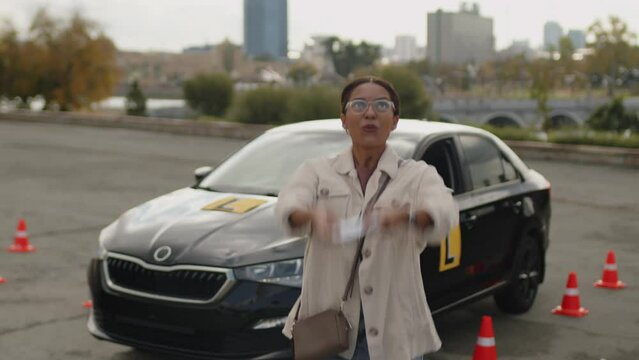 Medium portrait of happy young woman standing near black car cheerfully tearing yellow learners plate after passing driving test