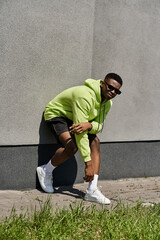 Stylish African American man in green hoodie leaning against a wall.