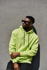 Handsome African American man leans against a wall in a lime green hoodie.