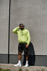 Stylish man in neon hoodie and shorts leaning against a wall.