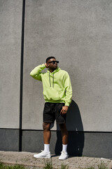Obraz premium Stylish man in neon hoodie and shorts leaning against a wall.