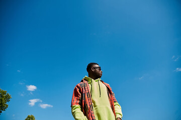 A fashionable African American man standing in a field under a blue sky.