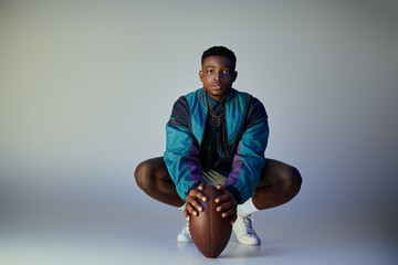 A stylish, athletic African American man crouching with a football.