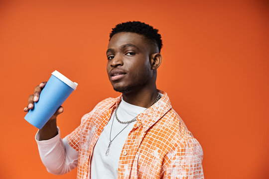 Handsome young man enjoying a hot cup of coffee against a vibrant orange backdrop.