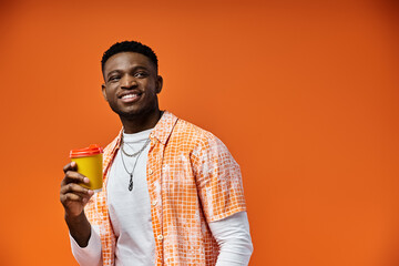 Handsome African American man enjoying a cup of coffee against a bright orange backdrop.