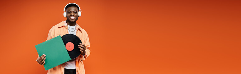 Young African American man in fashionable attire holding a vinyl record in orange backdrop.