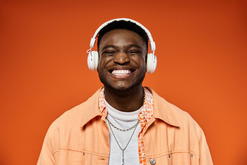 Handsome African American man with headphones beaming against orange backdrop.