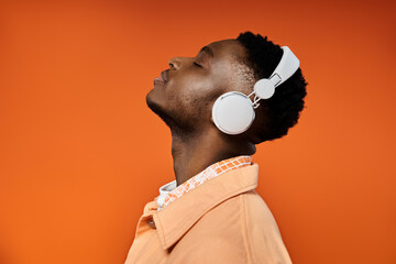 Stylish young man with headphones gazes at orange background.